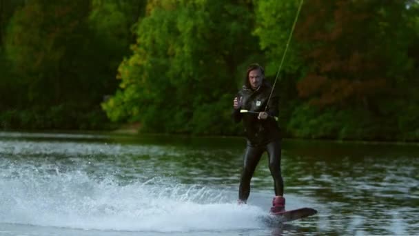 Mannen wakeboarder gör tecken av händerna under rörelse på floden bakom båten — Stockvideo