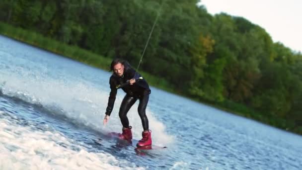 Guy spěchá podél jezera lesa na wakeboard dotýká vodní plochy ručně — Stock video