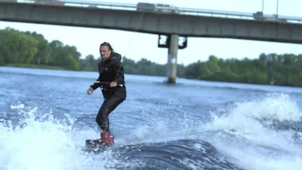 Man wakeboarding on river waves under city bridge in slow motion — Stock Video