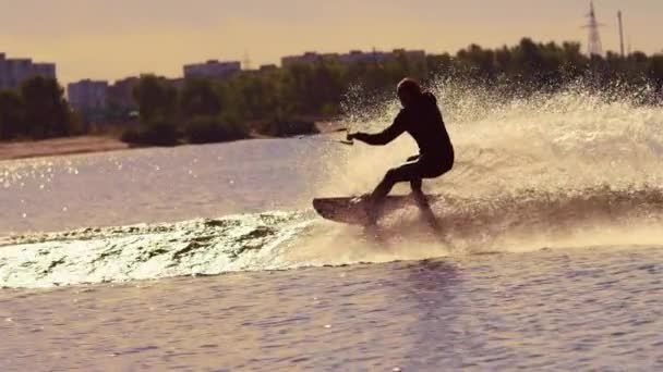 Hombre wakeboarding en el agua al atardecer. Wakeboarder haciendo trucos — Vídeos de Stock