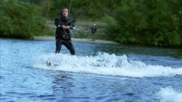 Feliz hombre wakeskier hacer señales por las manos durante el movimiento en el lago detrás del barco — Vídeo de stock