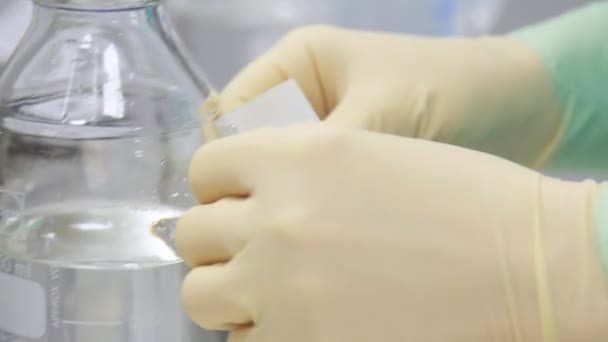 Laboratory worker sticking sticker at bottle with transparent liquid — Stock Video