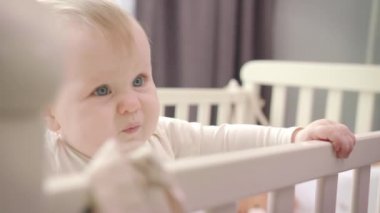 Üzgün bebek yatakta duruyor. Bebeklik duygusu. Küçük kız yatakta ayakta durmayı öğreniyor.