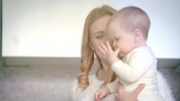 Matka se usmívá na dítě v bílém pokoji. Máma šťastná s dítětem — Stock video