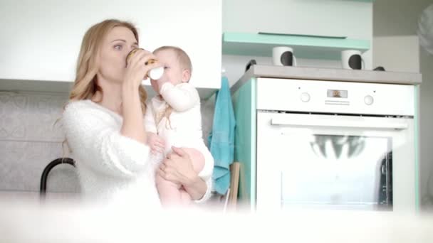 Madre bebiendo café y sosteniendo al bebé en la cocina. Permiso de maternidad — Vídeo de stock