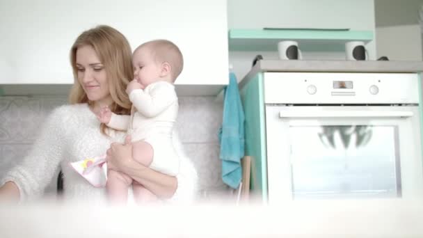 Mamá con el bebé va en la cocina blanca. Mujer de belleza con un niño pequeño en la mano — Vídeo de stock