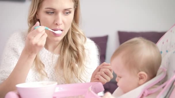 Blondine vrouw voedt kind met lepel. Moeder voeden baby met gepureerd voedsel — Stockvideo