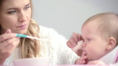 Genç anne bebeği besliyor. Genç anne çocuğu kaşıkla besliyor.