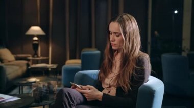 Otel lobisinde cep telefonundan mesaj yazan yorgun bir iş kadını.