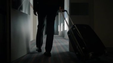Seyahat valizli bir iş adamı otel koridorunda yürüyor. Otele gelen adam