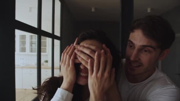 Egy fiatal család portréja, amint belépnek a házba. Mosolygó férfi becsukja a szemét a nő előtt. — Stock videók