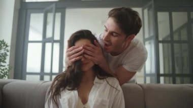 Erkek, elleri olan bir kadının gözlerini kapatıyor. Gülümseyen çift dizüstü bilgisayara bakıyor
