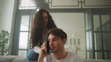Evde konuşan odaklanmış iş adamı. Kanepede zıplayan neşeli kadın.