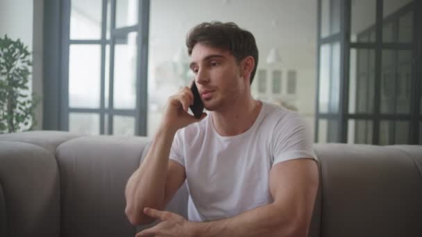 Hombre de negocios serio hablando de teléfono móvil en casa. Pareja joven abrazándose en el sofá . — Vídeo de stock