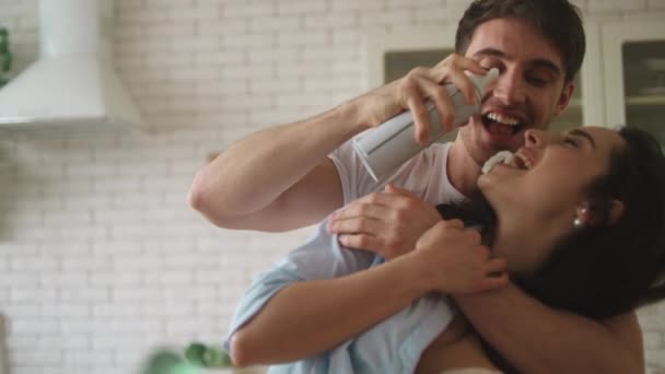 Joven pareja casada jugando con crema batida en casa . — Vídeos de Stock