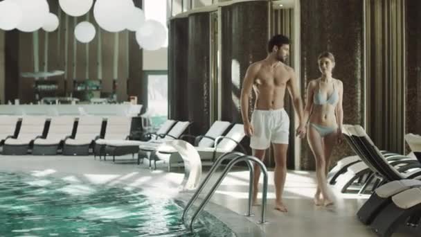 Молодая пара гуляет в закрытом бассейне в роскошном отеле. Держась за руки. — стоковое видео