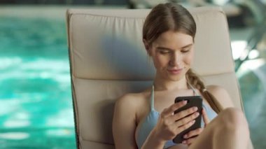 Havuzda telefonla rahatlayan seksi bir kadının portresi. Güzel kız kayan cep telefonu
