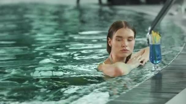 Close up feminino relaxante com coquetel na piscina. Mulher nadando na piscina de spa interior — Vídeo de Stock