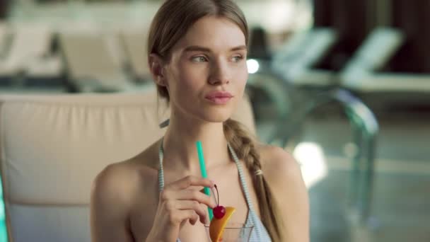 Porträt einer jungen Frau, die am Pool einen Cocktail trinkt. Frau flirtet in Liege. — Stockvideo