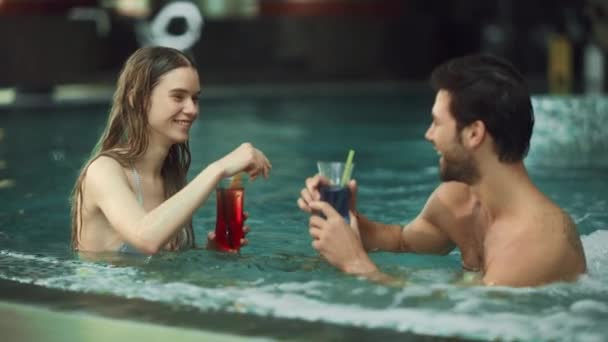 Крупным планом сексуальная пара отдыхает в бассейне спа. Счастливые мужчина и женщина наслаждаются напитками — стоковое видео
