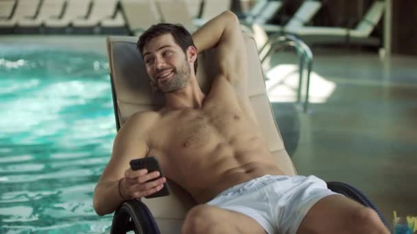 Primer plano hombre alegre utilizando el móvil en la piscina. Hombre feliz relajándose con el teléfono — Vídeo de stock