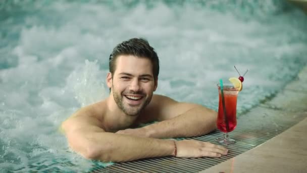 Retrato de un chico sexy relajándose en la piscina en el hotel spa. Hombre feliz posando en jacuzzi — Vídeos de Stock