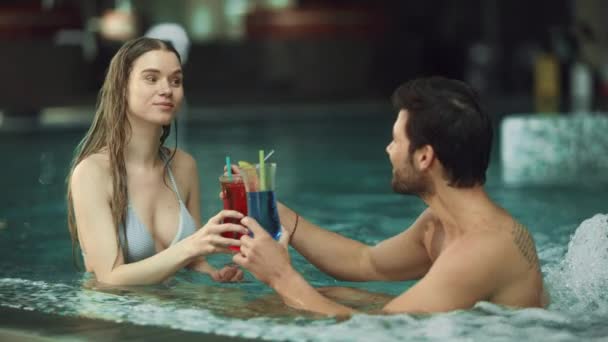 Close-up de jovem casal descansando na piscina. Homem e mulher felizes bebendo coquetéis — Vídeo de Stock