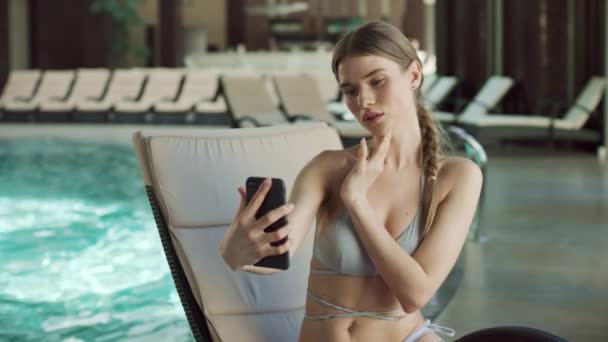 Portrait of young woman making selfie on lounger near swimming pool. — Stock Video