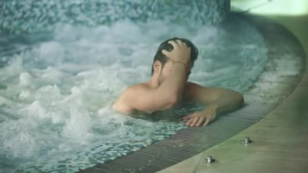 Όμορφος τύπος που ξεκουράζεται στο σπα του τζακούζι. Ελκυστικός άνθρωπος χαλαρώνοντας στο μπάνιο με υδρομασάζ — Αρχείο Βίντεο
