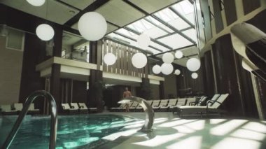 Kapalı havuzda yürüyen çekici bir adam. Adam yüzme havuzunun yanında dinleniyor..