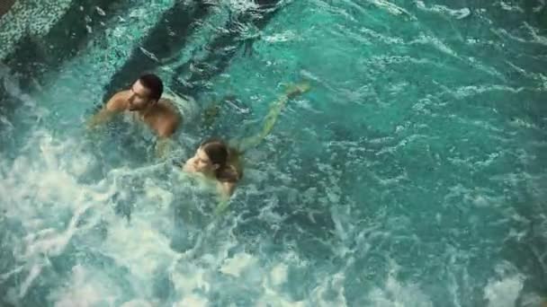 Vonzó pár pihennek pezsgőfürdőben. Szép pár úszik a medencében. — Stock videók
