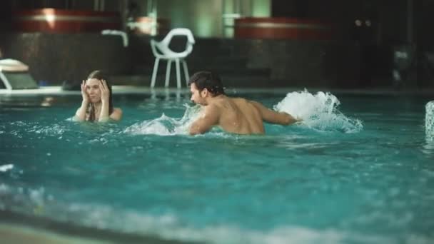 Casal sorridente salpicando na piscina do hotel. Alegre casal se divertindo na água — Vídeo de Stock