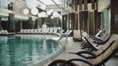 Otelde su havuzunun yanında yürüyen yakışıklı bir adam. Formda bir adam spa havuzunun yanında dinleniyor..