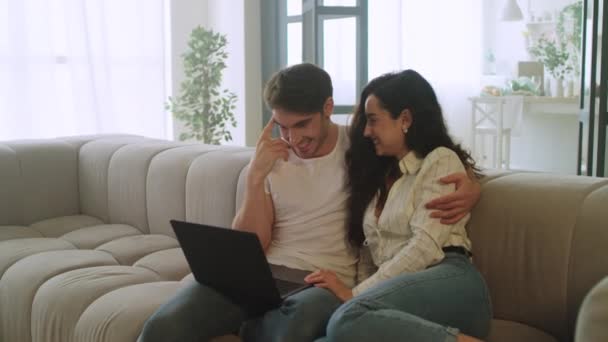 Pareja feliz viendo el portátil en casa. Joven hombre y mujer relajarse en el sofá — Vídeo de stock