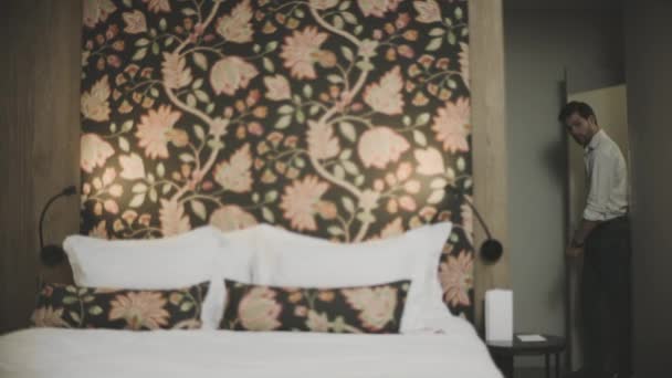 Trött man kommer in i rummet på lyxhotell. Sexig kille hoppar säng i moderna sovrum — Stockvideo