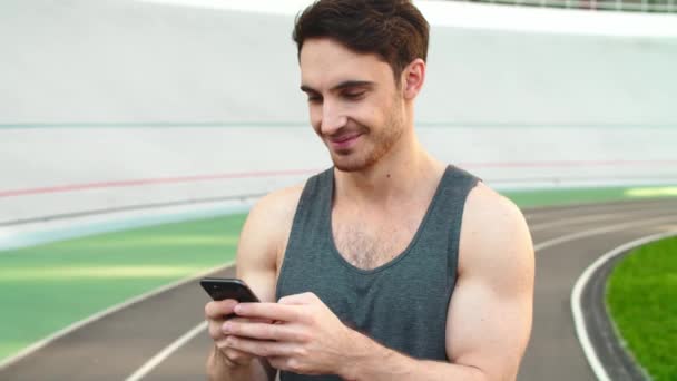 Nahaufnahmeläufer steht mit Smartphone auf der Strecke. Sportlicher Mann mit Handy — Stockvideo