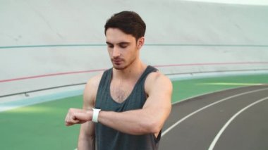 Adam koşucu stadyumda akıllı saate bakıyor. Genç koşucu sonuçları kontrol ediyor