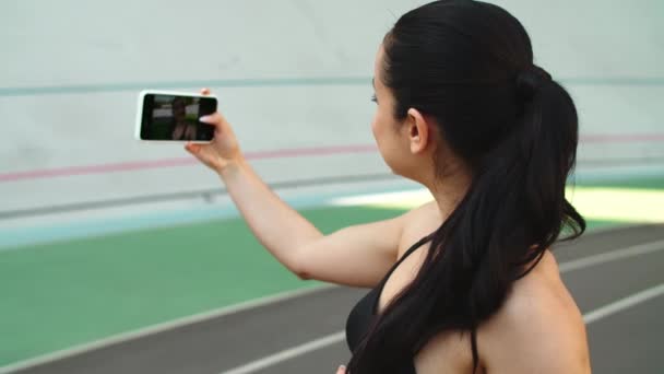 Atletisk kvinna som tar selfie foto på mobiltelefon på sportbanan — Stockvideo