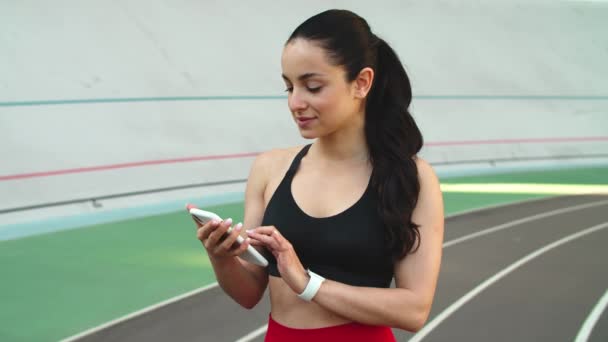 Retrato de menina fitness usando telefone no estádio. Mulher do esporte com smartphone — Vídeo de Stock