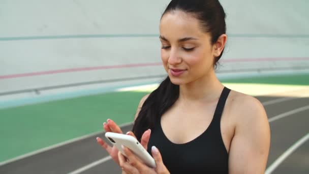 Chica deportiva usando el teléfono móvil en el estadio. Deportiva mujer comprobar resultados — Vídeos de Stock