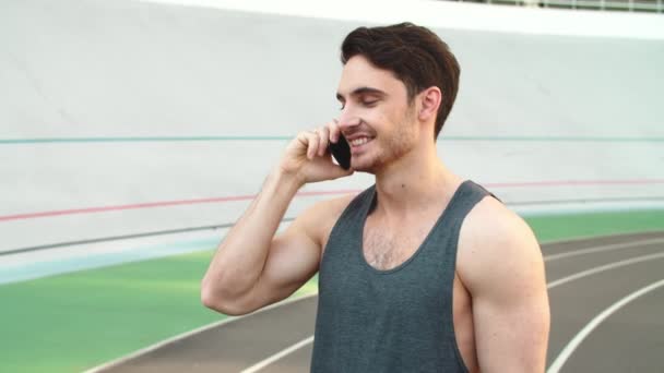 Portrait of attractive runner male talking on phone on track — Stock Video