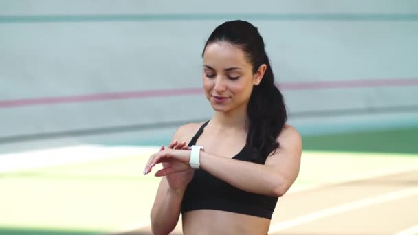 Πορτρέτο της γυμναστικής γυναίκα έλεγχο των αποτελεσμάτων σε έξυπνο ρολόι στο γήπεδο του αθλητισμού — Αρχείο Βίντεο