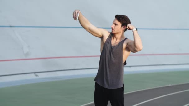 Спортивный человек сгибает мышцы для селфи фото на современном треке — стоковое видео