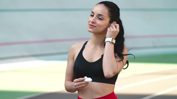 Sportowa kobieta nosząca słuchawki na nowoczesnym torze. Pasująca kobieta słuchająca muzyki na świeżym powietrzu — Wideo stockowe