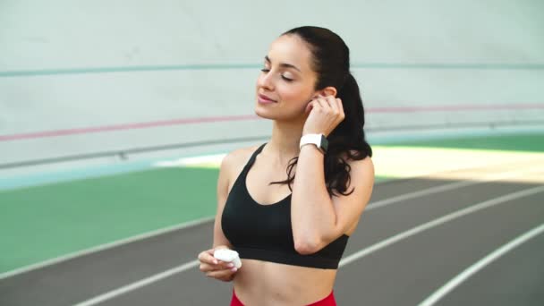 Mulher do esporte usando fones de ouvido na pista no estádio. Mulher fitness em fones de ouvido — Vídeo de Stock
