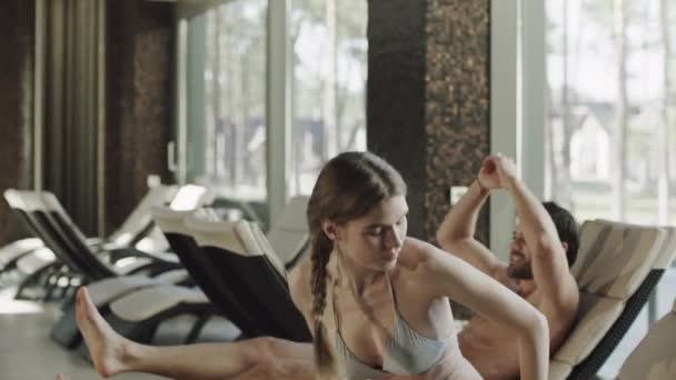Primer plano sexy pareja sentado en la tumbona cerca de la piscina cubierta . — Vídeos de Stock
