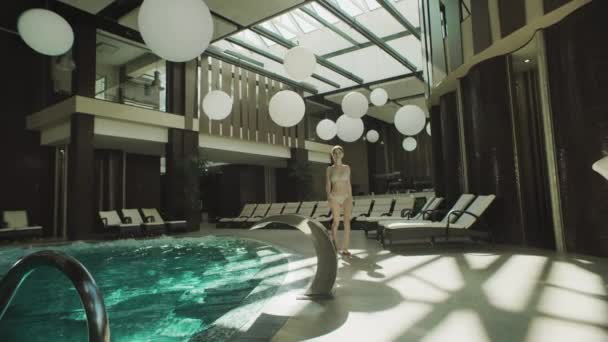 Menina sexy andando ao longo da piscina em biquíni. Mulher bonita flertando piscina interior. — Vídeo de Stock