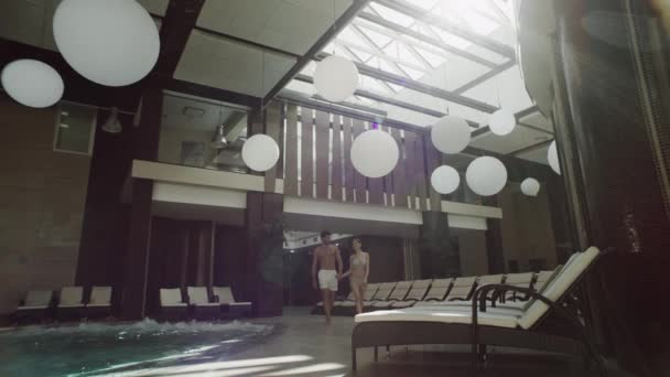 Romantic couple walking indoor pool. Happy couple holding hands poolside — Stock Video