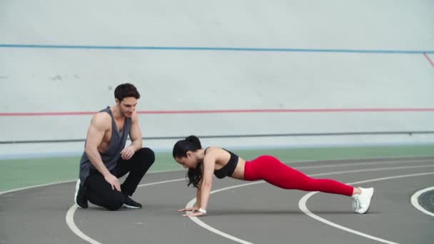Een vrouw die push-ups doet in het sportstadion. Paar trainingen samen in het sportstadion — Stockvideo