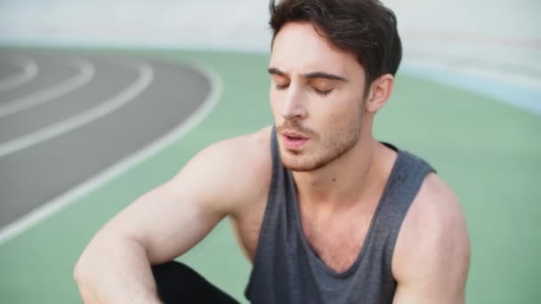 Atleet man rusten na het sporten in het stadion. Moe loper zittend op het circuit — Stockvideo